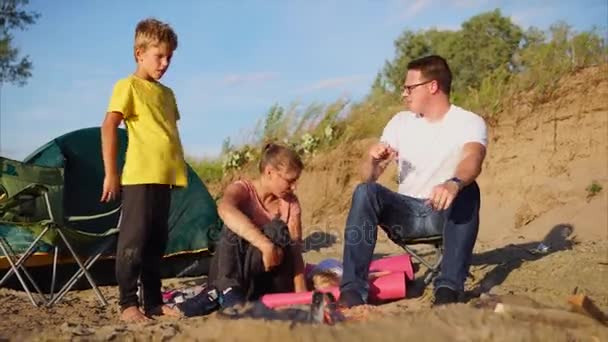 Ung familj med ett barn är uppvärmningen runt en eld och tält på natur på sommaren — Stockvideo