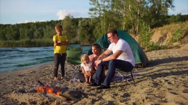 Padres e hijos calentándose junto al fuego en el campamento — Vídeos de Stock