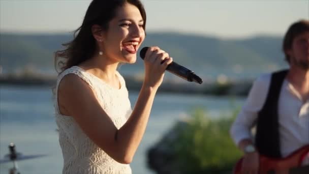 Una chica joven y bonita canta una canción enérgica en un micrófono al aire libre — Vídeos de Stock