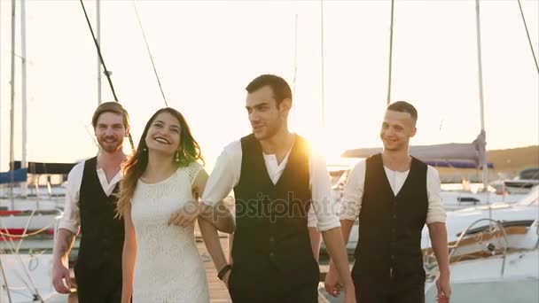 Jonggehuwden en vrienden van een vriend wandeling langs de pier waar er een boten — Stockvideo