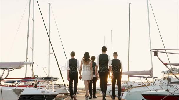 Группа людей в официальной одежде идет вдоль пирса, где стоят яхты — стоковое видео