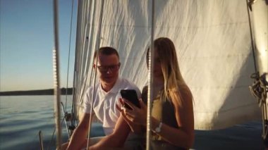 Genç erkek ve kadın resimleri smartphone, yelkenli üzerinde oturan değerlendiriyorlar