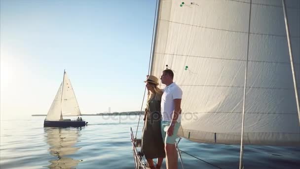 Pareja joven está de pie en una nariz de velero en un día soleado, mirando un mar — Vídeos de Stock