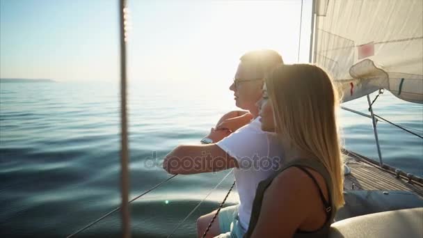 Joven hombre y mujer con el pelo rubio están sentados en un yate en un día soleado tranquilo — Vídeos de Stock