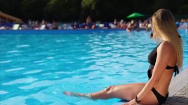 Güzel genç kadın havuz kenarında oturuyor.