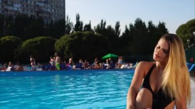 Güzel genç kadın havuz kenarında oturuyor.