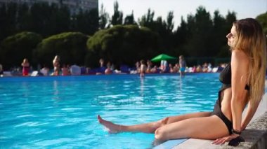 Güzel genç kadın havuz kenarında oturuyor.