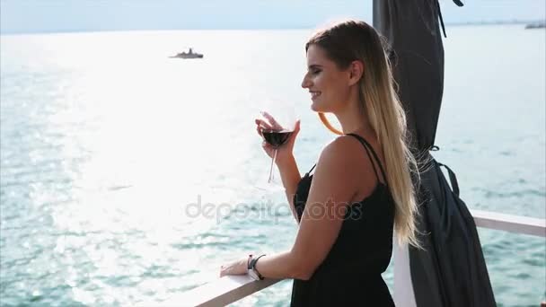 Vacker kvinna står på terrassen med ett glas vin. — Stockvideo