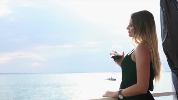 Mladá žena červené víno pije a vypadá na moře, lady jezdí lodě na vodě — Stock video