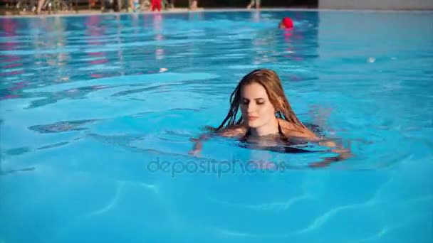 Rubia tentadora con el pelo largo y húmedo está nadando hasta el lado de la piscina . — Vídeo de stock