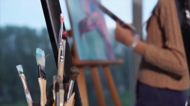 Um artista pinta um quadro de um flamingo na frente são pincéis manchados com tinta — Vídeo de Stock