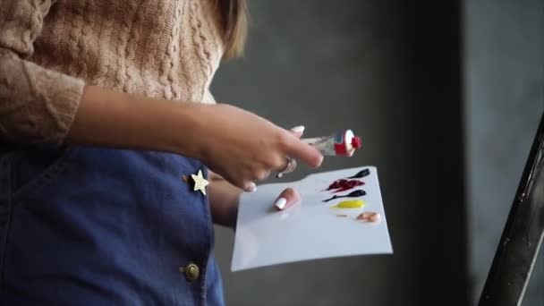 Primer plano de las manos de una mujer que aprieta pintura en una paleta blanca — Vídeo de stock