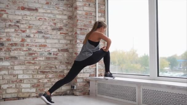 Mujer joven haciendo estiramiento de los músculos de las piernas apoyados en el alféizar de la ventana — Vídeos de Stock