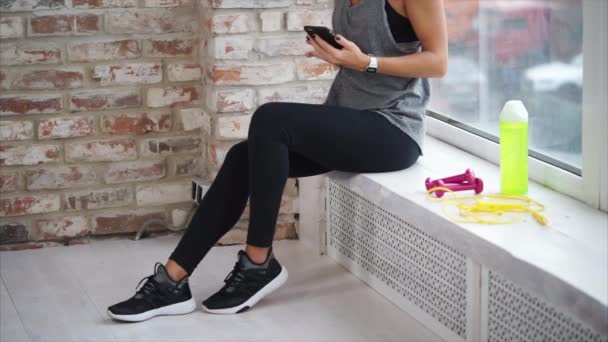 Una mujer se corresponde con sus amigos en un teléfono móvil después del entrenamiento físico — Vídeo de stock