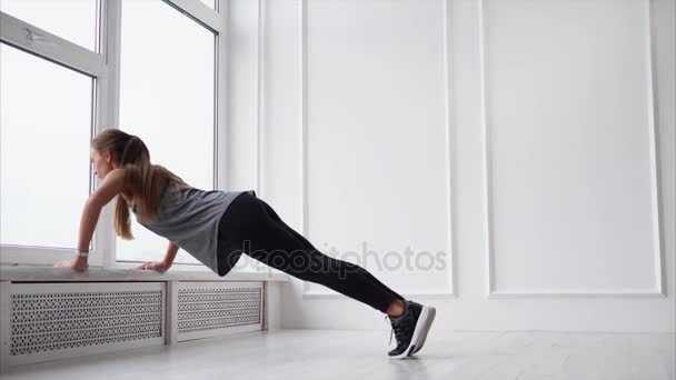 Молодая спортсменка отжимается на подоконнике в светлой комнате . — стоковое видео