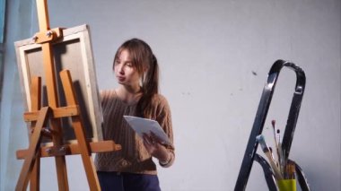 Genç kadın büyük pencereler ile sanat alanda tuval üzerine yağlı boya resim yapıyor.