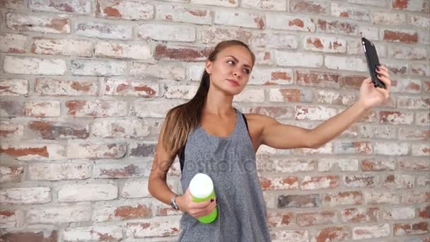 Girl dressed in sportswear is taking selfie by phone near brick wall in a gym — Stock Video