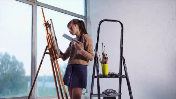 Joven pintor está dibujando en el estudio de arte, de pie cerca de grandes ventanas . — Vídeos de Stock