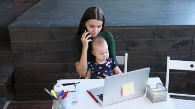Notlar ve ofiste bir çocuk tutan bir smartphone cep telefonu ile konuşurken kadın
