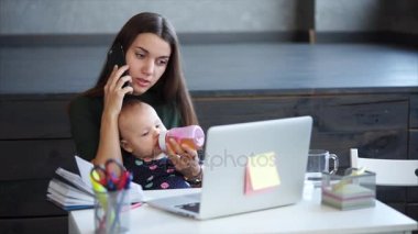 Yetişkin kadın bir evde bir diz bebek tutan cep telefonuyla konuşuyor.