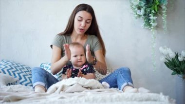 Genç esmer anne ve bebek kız yatağa oturmuş ve alkışlar.