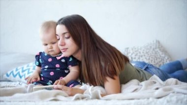 Çekici bir kadın ve onun sevimli bebek yatakta yatmak ve cep telefonu üzerinde çizgi film izlemek