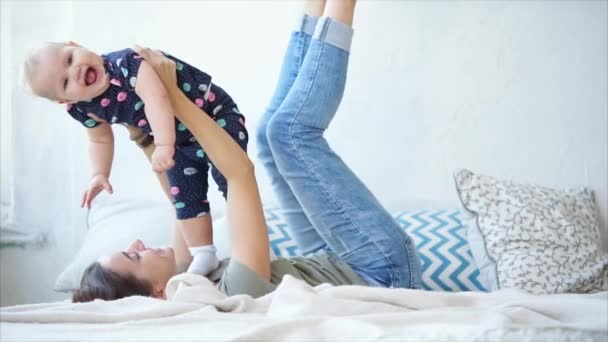Mujer feliz está jugando con su bebé en un dormitorio durante el día . — Vídeos de Stock