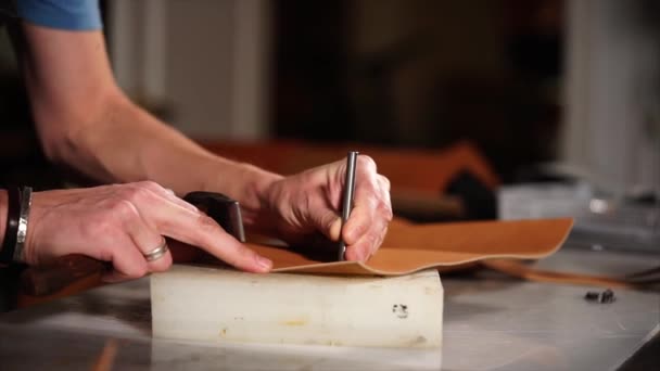 Close up shot of an employees hands, who makes holes with a hammer in a eather — Stock Video