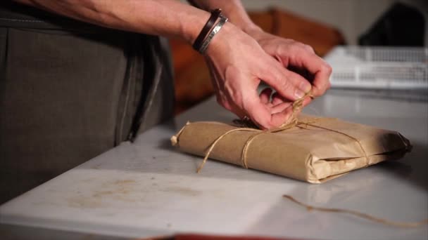 Крупним планом знімок чоловічих рук, які акуратно упаковують товари в крафт-папір — стокове відео