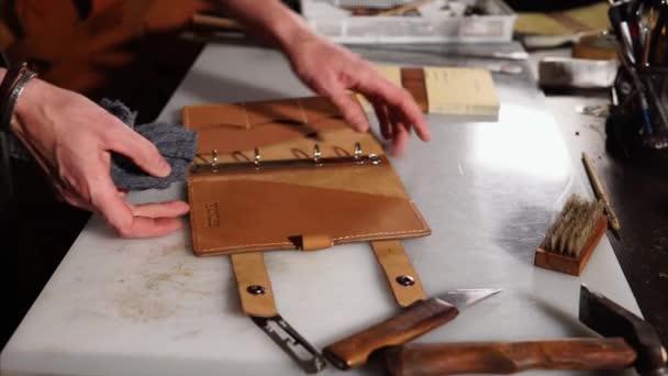 Homem está esfregando arte de capa de couro acabado para livro em uma mesa em seu estúdio — Vídeo de Stock