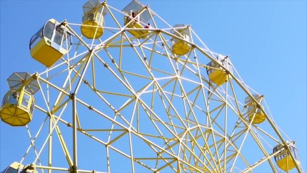 Ярко-желтое старое колесо обозрения движется на фоне ясного голубого неба — стоковое видео
