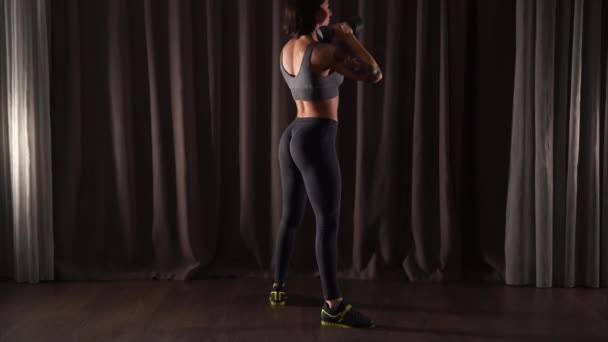 Deportiva morena chica está haciendo sentadillas con mancuernas en un gimnasio oscuro — Vídeos de Stock