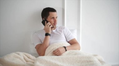 Yetişkin bir adam bir yatakta yatıyor, sonra iş ortağı ile bir akıllı telefon konuşması