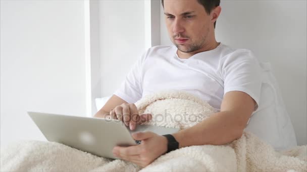 Hombre guapo en la cama con un portátil — Vídeo de stock