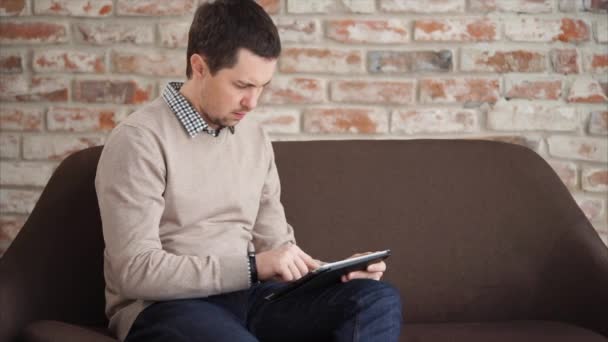 The man prints text on a tablet, he holds a gadget in hand and uses the Internet — Stock Video