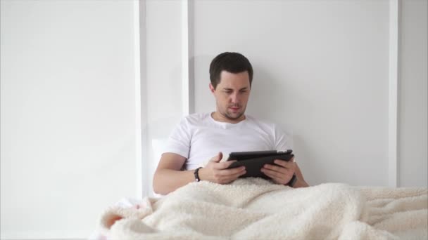 Homme avec du chaume couché au lit avec une tablette . — Video