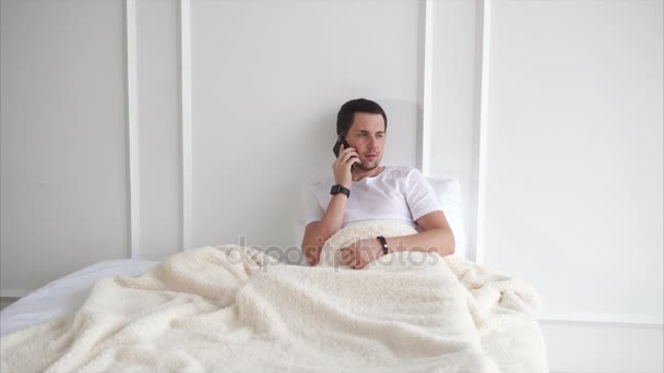 Mężczyzna rozmawia z kolegą, leżąc w łóżku. — Wideo stockowe