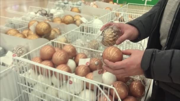 Hombre eligiendo bolas de árbol de Navidad en el hipermercado — Vídeos de Stock