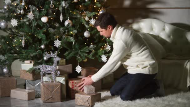 Gelukkig vader verbergt geschenkdozen onder de kerstboom — Stockvideo