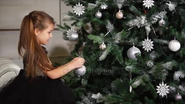 美しい少女がクリスマス ツリーにおもちゃをハングアップします。. — ストック動画