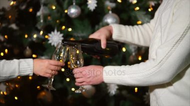 Erkek ve kadın şampanya yılbaşı ağacının yanında duran bardaklarda yağıyor