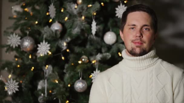 Felnőtt jóképű férfi díszített karácsonyfa közelében állt, és mosolyogva — Stock videók