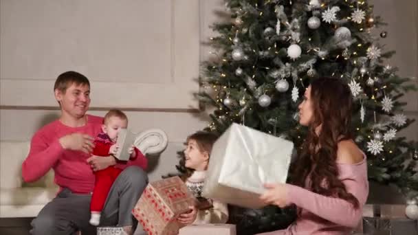 Дети с родителями сидят рядом с большой новогодней елкой и кучей подарков . — стоковое видео