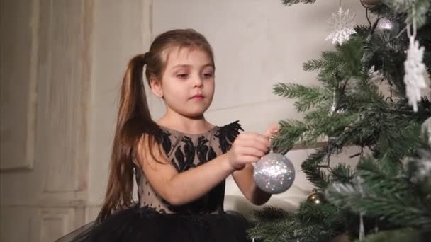 Feliz niña está decorando el árbol de Año Nuevo y jugando con una pelota — Vídeo de stock