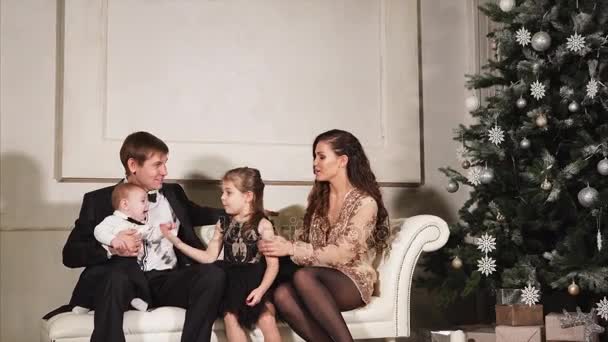 Familia feliz está sentado en un sofá en la víspera de Navidad en el pasillo con abeto decorado — Vídeos de Stock