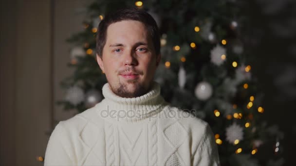 Retrato de un hombre tranquilo y contento en un suéter cálido que está frente a un árbol de Navidad — Vídeo de stock