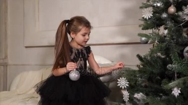 küçük kız bir Noel ağacı tatil öncesi elbise, çocuk şube parlak topları üzerinde asılı
