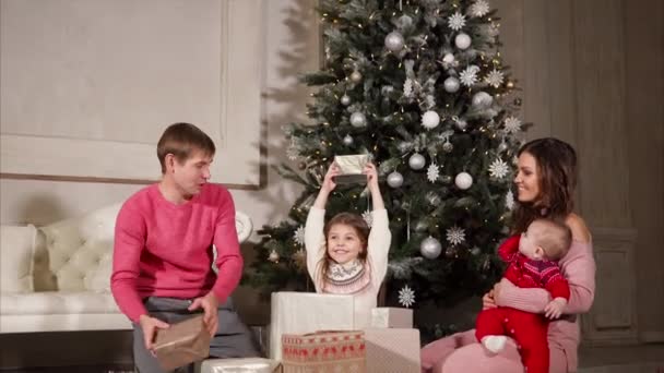 Familjen ger varandra presenterar under det nya året, de sitter nära julgranen — Stockvideo