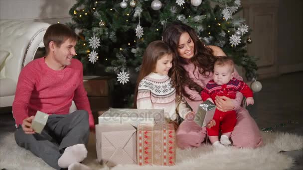 Familia joven sentada en el suelo cerca del árbol de Navidad festivo y viendo regalos de Año Nuevo — Vídeos de Stock