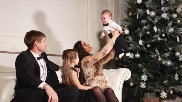 Une famille jeune et heureuse en costumes de fête joue avec leur petit fils près de l'arbre du Nouvel An — Video